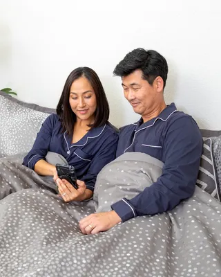 Husband and wife in blue pajamas look at a cell phone in bed