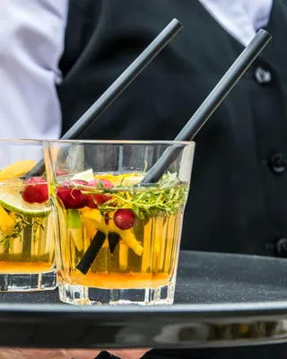 Two glasses of yellow beverage with garnishes on a server tray