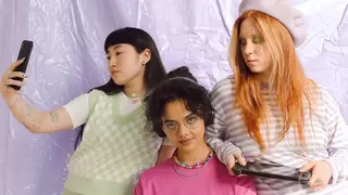 Three Gen Z youth in brightly colored clothes enjoy electronic devices