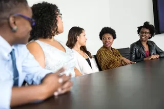 Professional women of color sit at a boardroom table