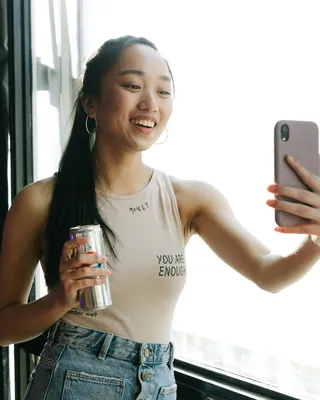 Young woman with long hair takes selfie photo with a canned beverage