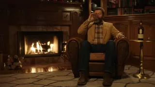 Nick Offerman sits by a fireplace in a dimly lit room